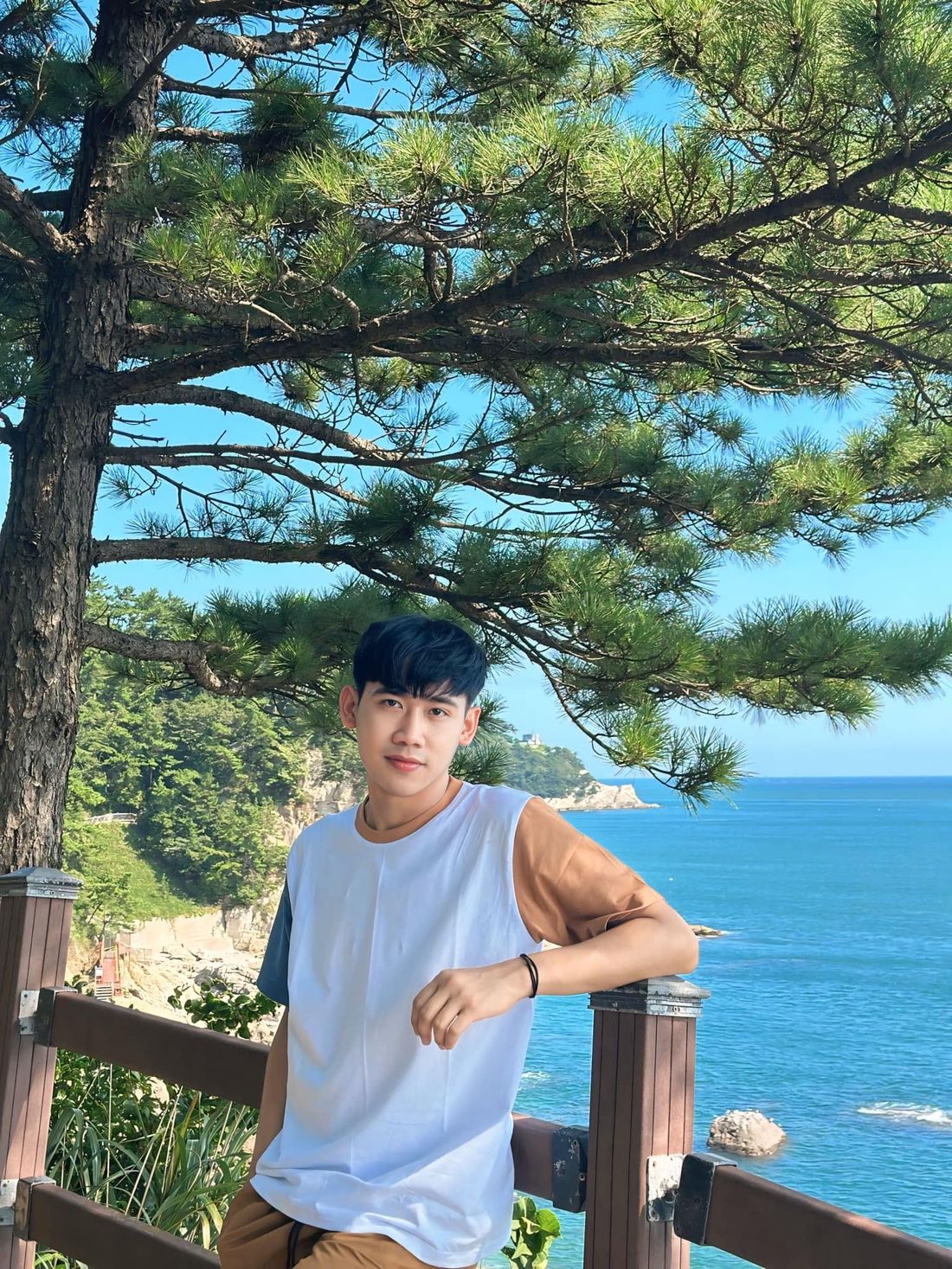 Portrait of Disma Putra Pramana standing by a wooden railing with the sea behind him